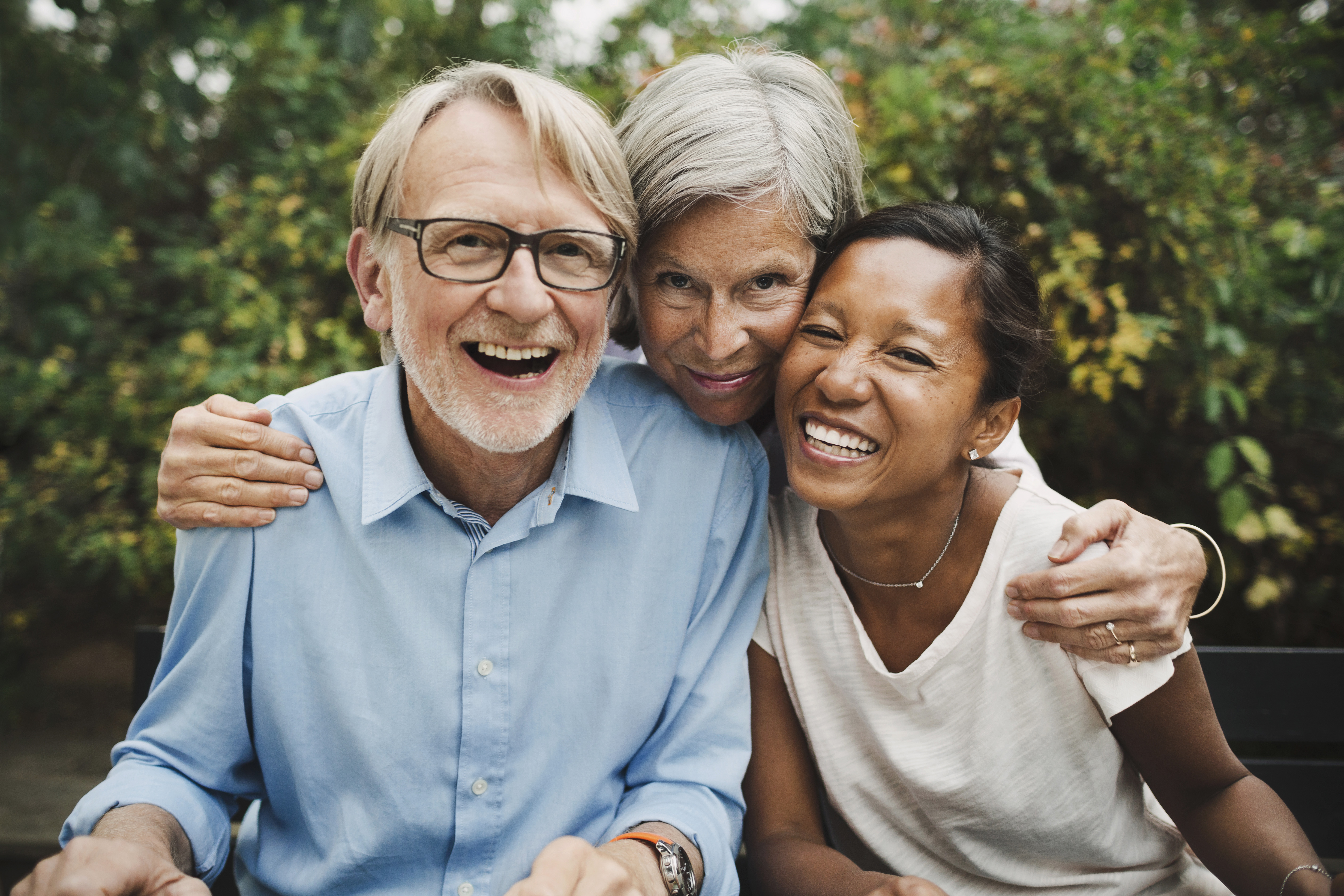 Elderly woman holding arms around a man and a woman, all smiling and looking into the camera