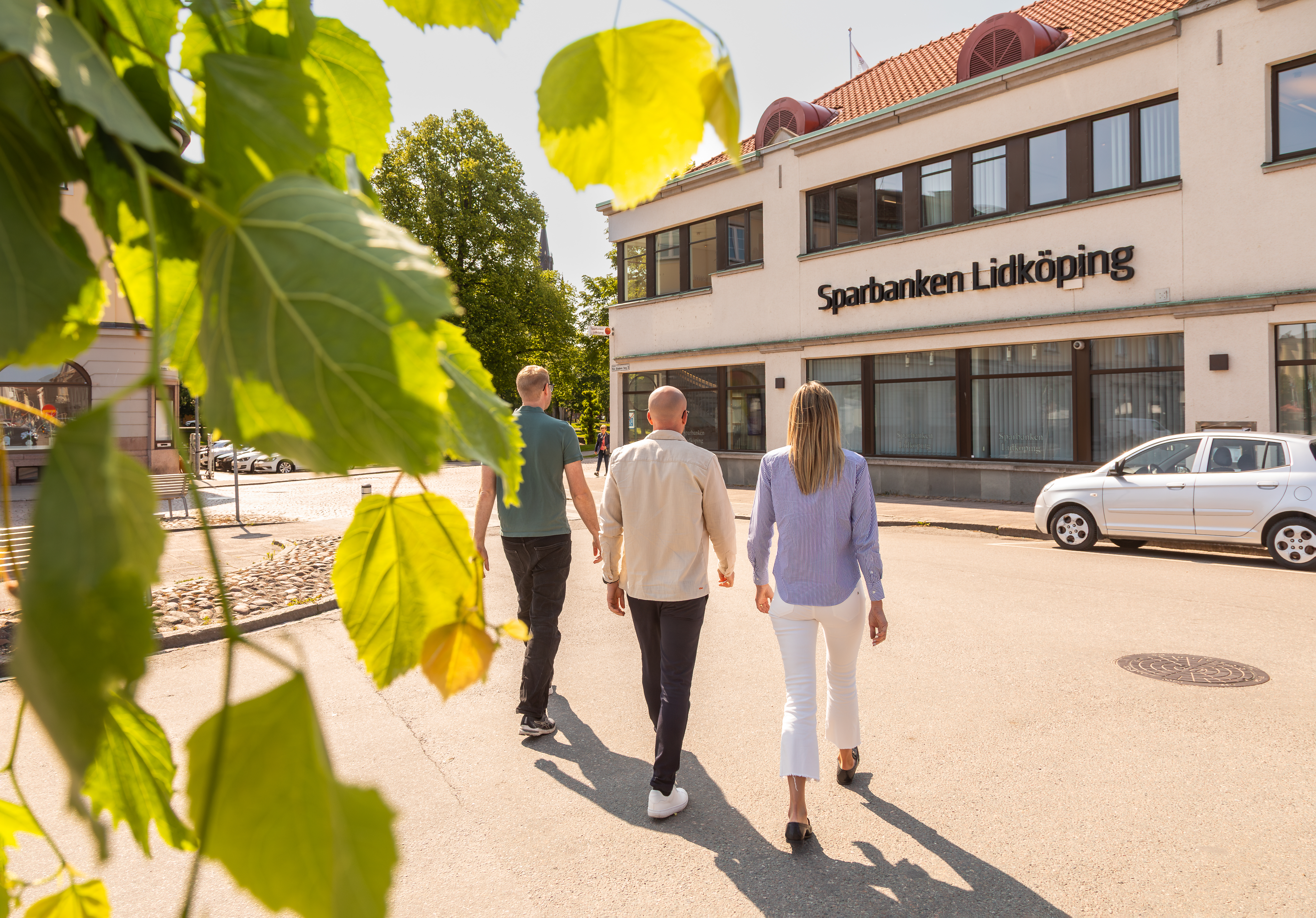 Tre personer går mot Sparbanken Lidköping i solsken
