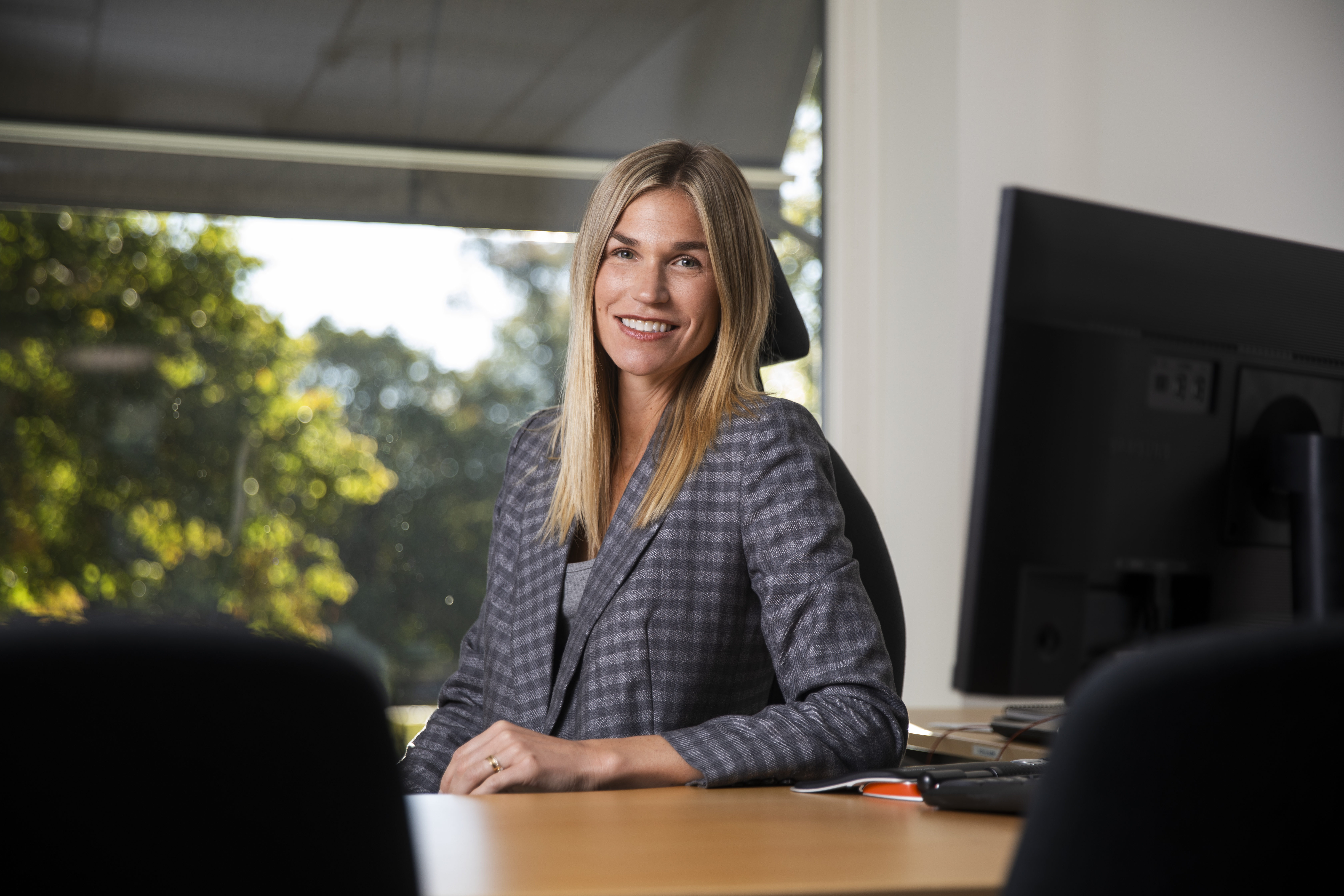 En kvinna sitter vid skrivbordet och ler in i kameran