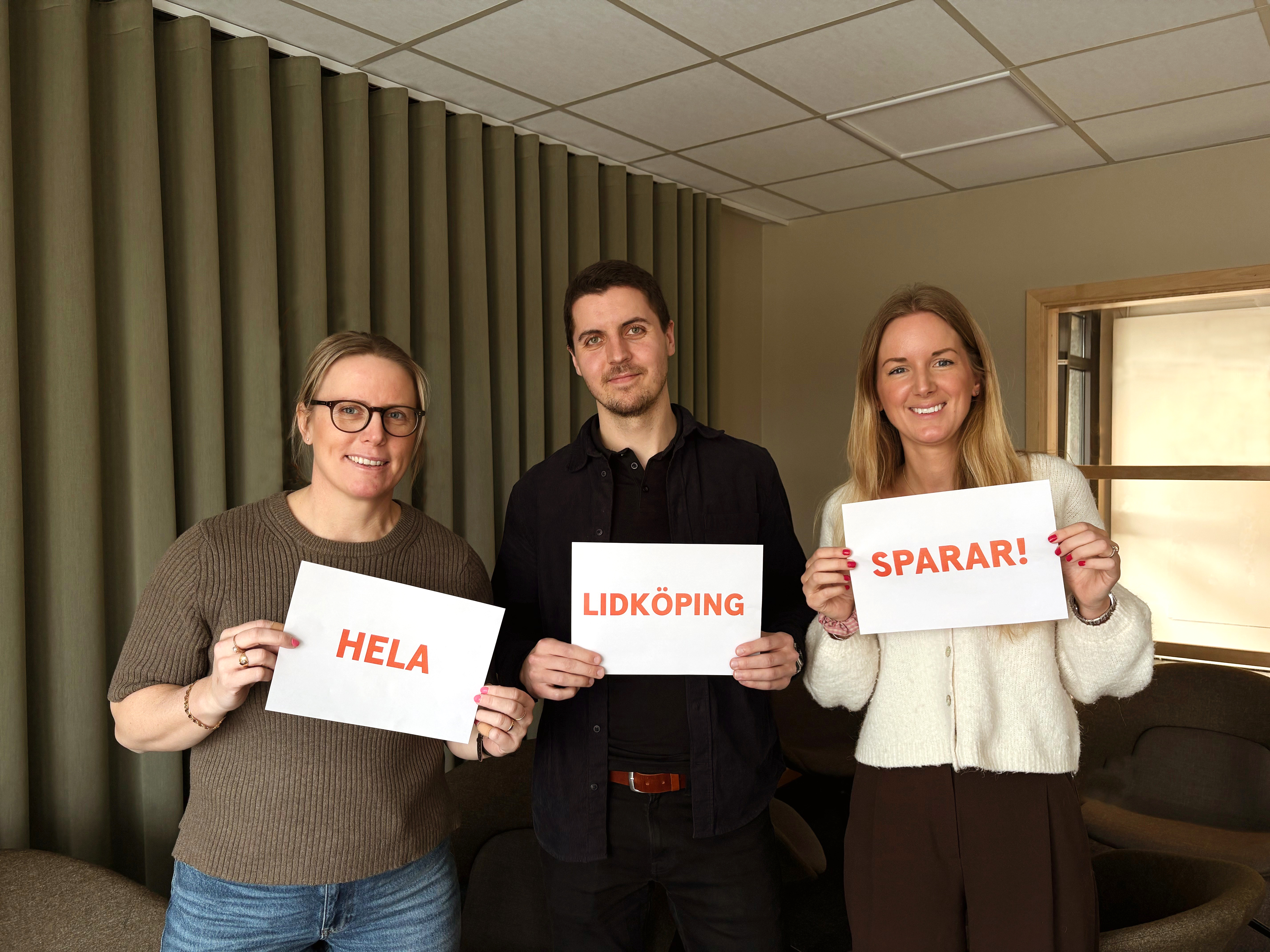 Tre kollegor som håller i skylt med budskapet Hela Lidköping sparar