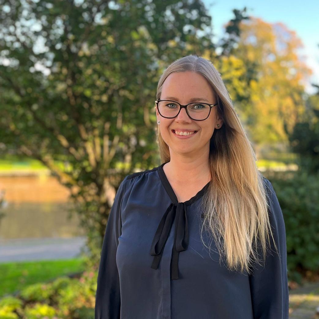 Kvinna står utomhus och ler mot kameran