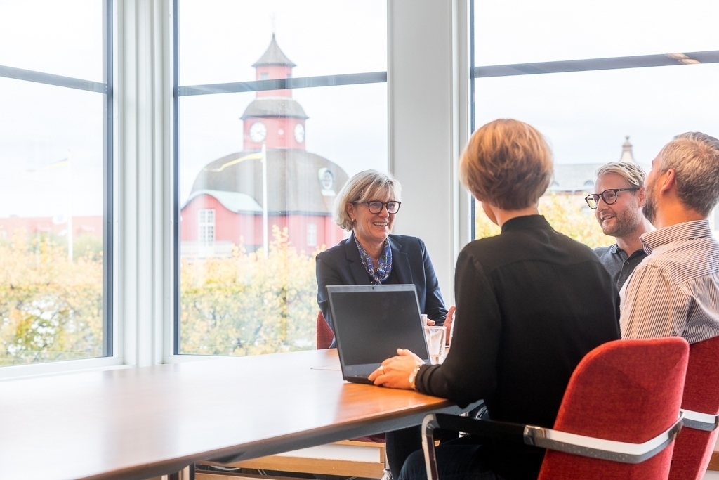 Fyra personer sitter vid ett bord med en dator och pratar med varandra
