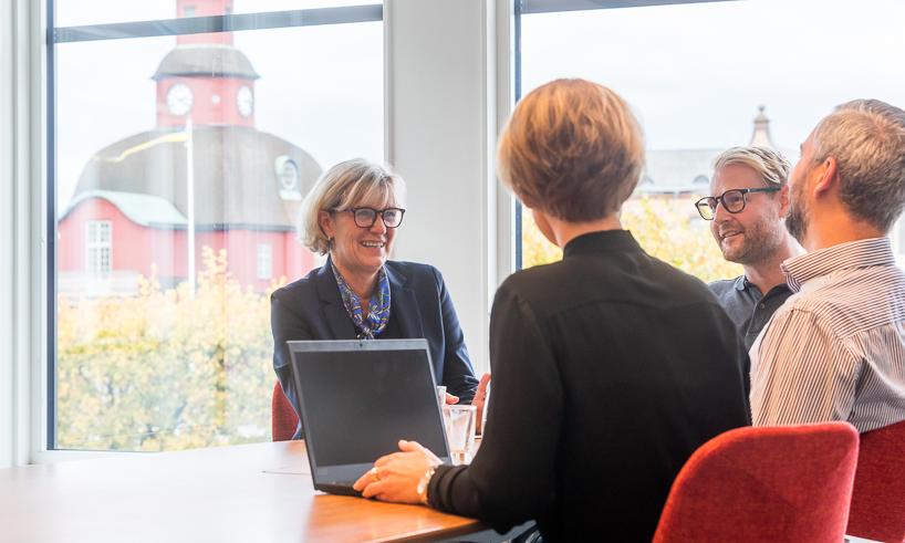 Fyra personer sitter vid ett bord med en dator och pratar med varandra