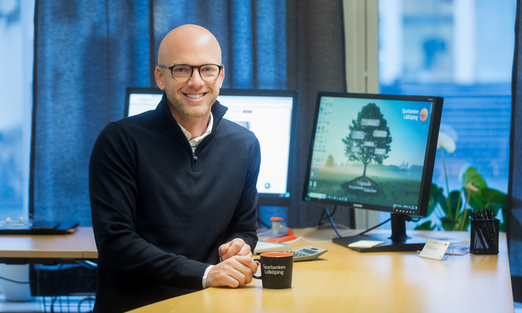 Man står vid sitt skrivbort och ler mot kameran 